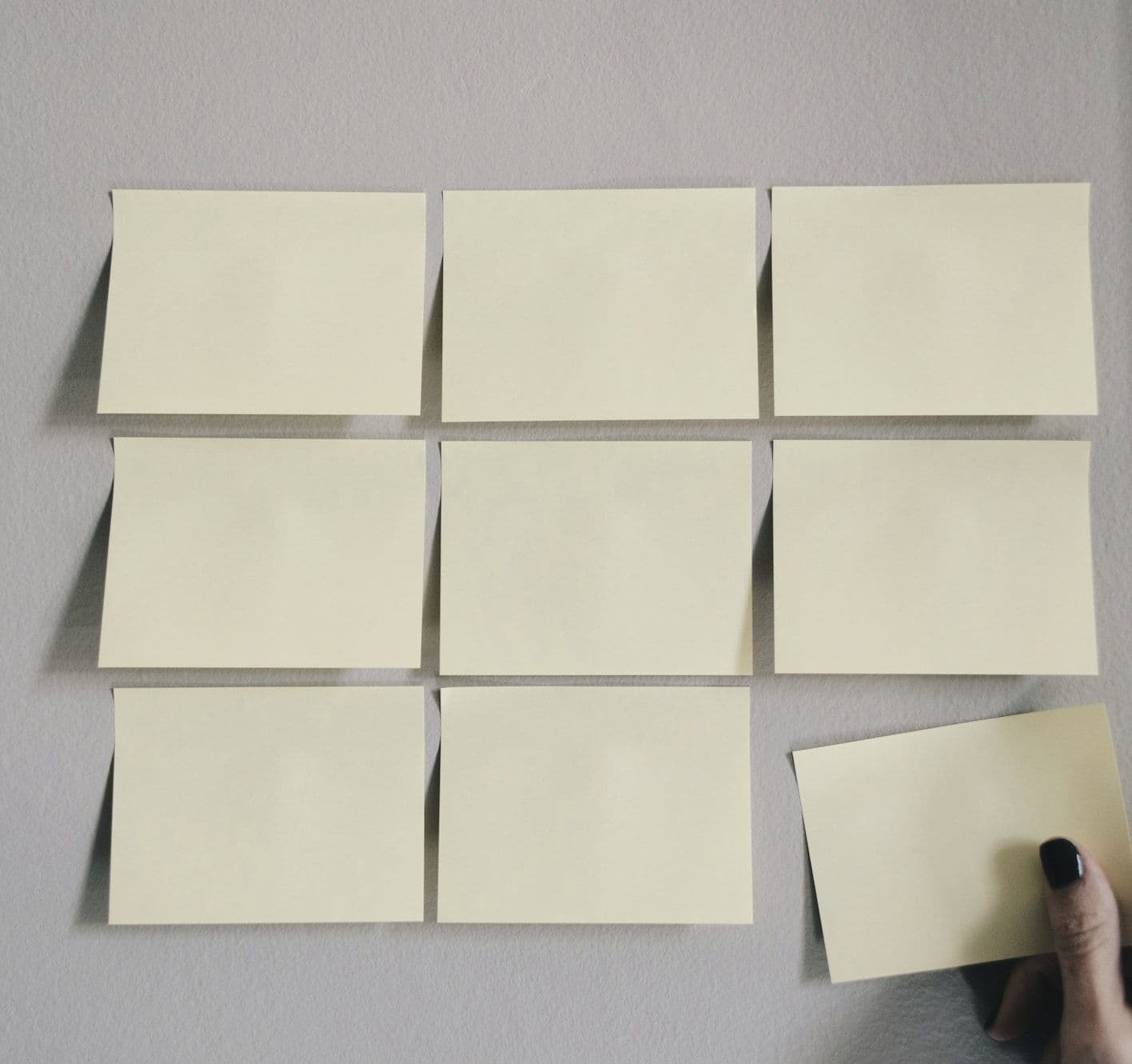 Hand placing sticky notes in a grid on a gray wall Hand placing sticky notes in a grid on a gray wall